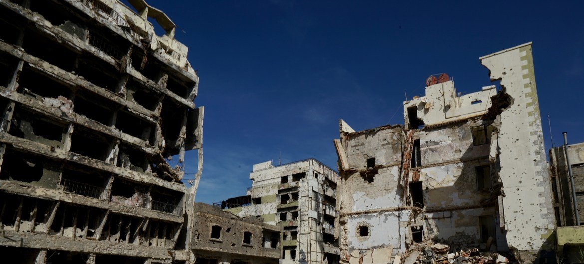 طفلان يسيران في شارع مهجور تصطف على جانبيه مبانٍ متضررة ومدمرة بشدة في بنغازي، ليبيا.