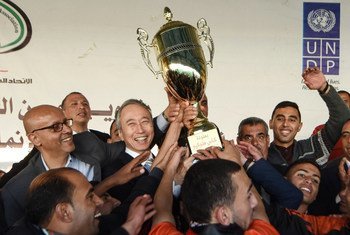 السفير الياباني تاكيشي أوكوبو، وممثل برنامج الأمم المتحدة الإنمائي يحملان كأس بطولة دوري طوكيو النهائية في غزة لتقديمه إلى فريق خان يونس الفائز بالبطولة.