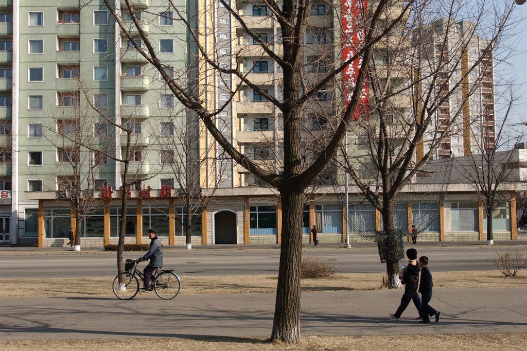 朝鲜儿童和成人经过首都平壤的一栋高层公寓楼。 2004年7月，城市住宅中的电力和水短缺十分普遍。