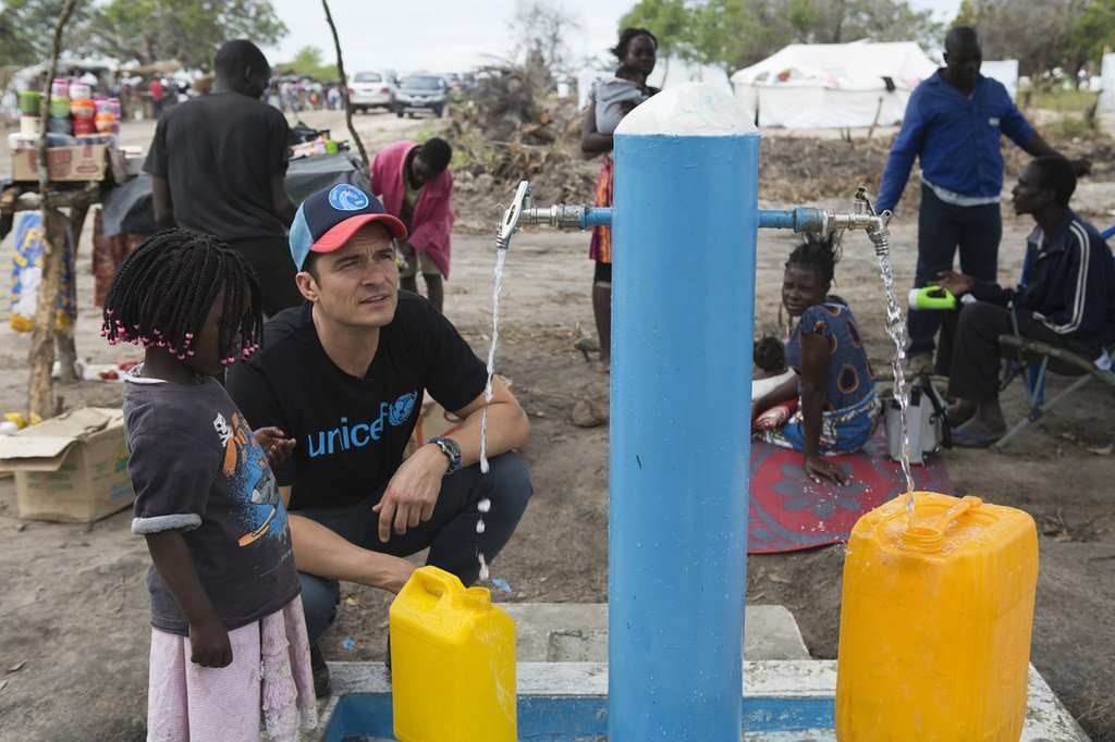 سفير النوايا الحسنة لليونيسف أورلاندو بلوم، يساعد طفلة على ملء وعاء بالمياه في موقع إعادة التوطين في ميندروزي للنازحين بسبب الأعاصير الأخيرة. في موزمبيق. 