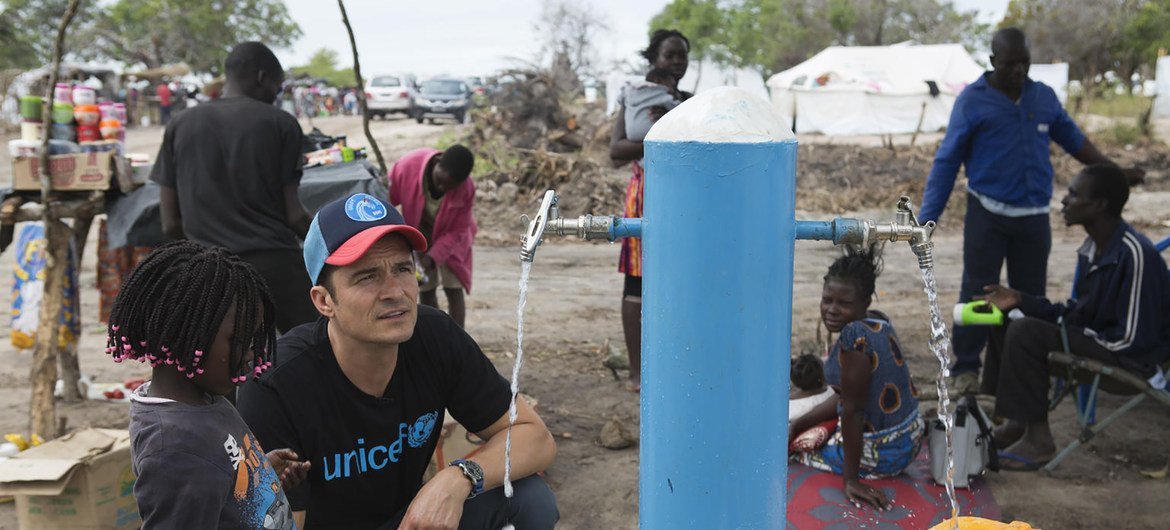 سفير النوايا الحسنة لليونيسف أورلاندو بلوم، يساعد طفلة على ملء وعاء بالمياه في موقع إعادة التوطين في ميندروزي للنازحين بسبب الأعاصير الأخيرة. في موزمبيق. 