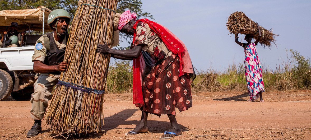 أحد أفراد قوات حفظ السلام التابعة للأمم المتحدة من إثيوبيا يساعد امرأة في تحميل الحطب على رأسها في جنوب السودان. (ملف 2015)