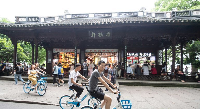 年轻人骑车经过中国杭州的西湖，西湖被列入教科文组织世界遗产名录。