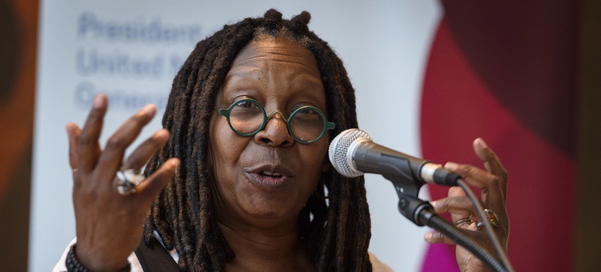 Whoopi Goldberg discursa em um pódio ao microfone durante um evento.