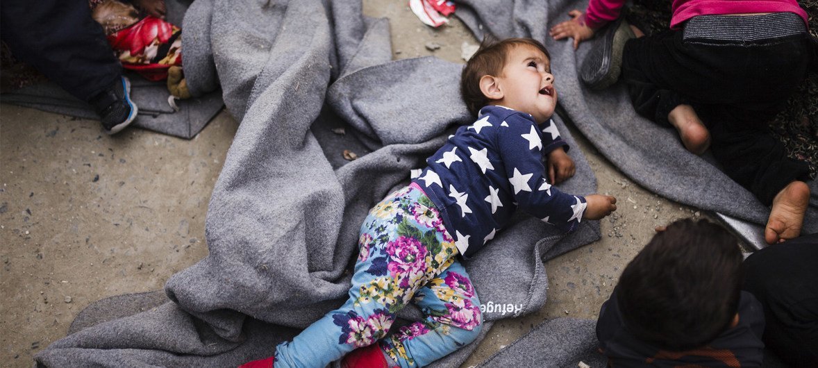 希腊的伊多梅尼临时难民营收容了成千上万渴望经由所谓的“巴尔干通道”前往西欧的移民与难民，一名年幼的难民女童垫着一条毛毯躺在马路中间。