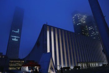 Sede da ONU em Nova York ao entardecer, com uma postura de ioga projetada na lateral do prédio da Secretaria para celebrar o Dia Internacional da Ioga.