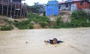 A young boy in Bangladesh navigates a river swollen from days of monsoon rain. He is collecting plastic bottles washed into the river to sell to recyclers to help his family purchase food. (July 2019)