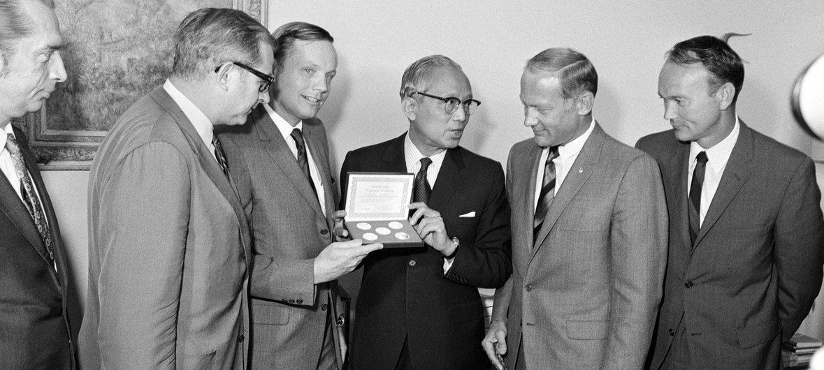 时任联合国秘书长吴丹向尼尔·阿姆斯特朗、迈克尔·柯林斯和巴兹·奥尔德林等来访者展示了一套联合国25周年纪念奖章。