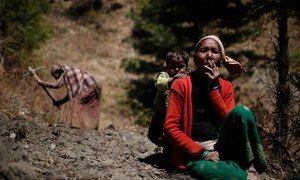 A woman, her child behind her, pauses in the field to smoke a cigarette in Sawa Khola Village, Mugu District.