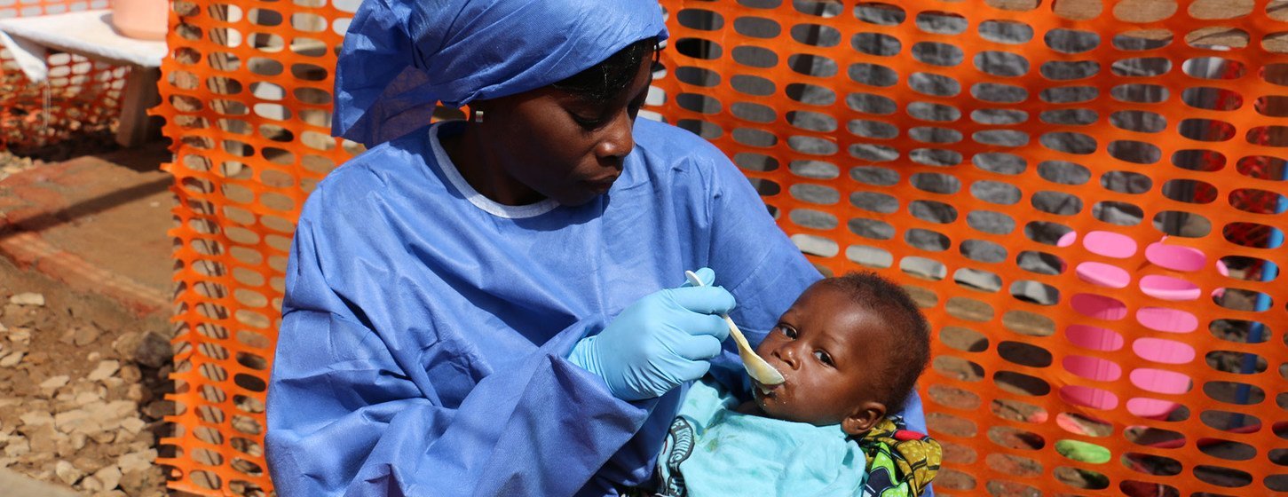 Un agent de santé en tenue de protection nourrit un bébé dans un centre de traitement contre Ebola à Beni, en RDC.